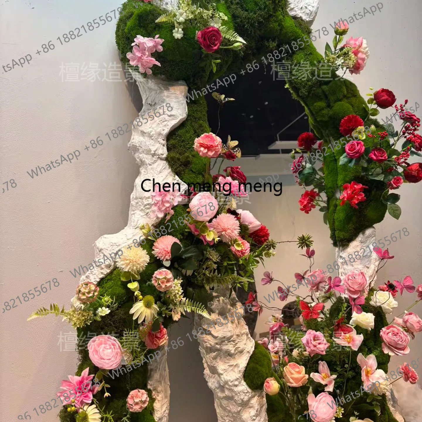 Baby Clothing Stores - a55 衣料品店の窓の装飾鏡が緑の植物の壁を飾り、コーヒーショップの雰囲気には花飾りが配置されています。